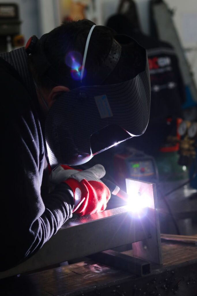 pexels-photo-9729626-9729626 Welder in protective gear welding metal in a workshop, emitting sparks.